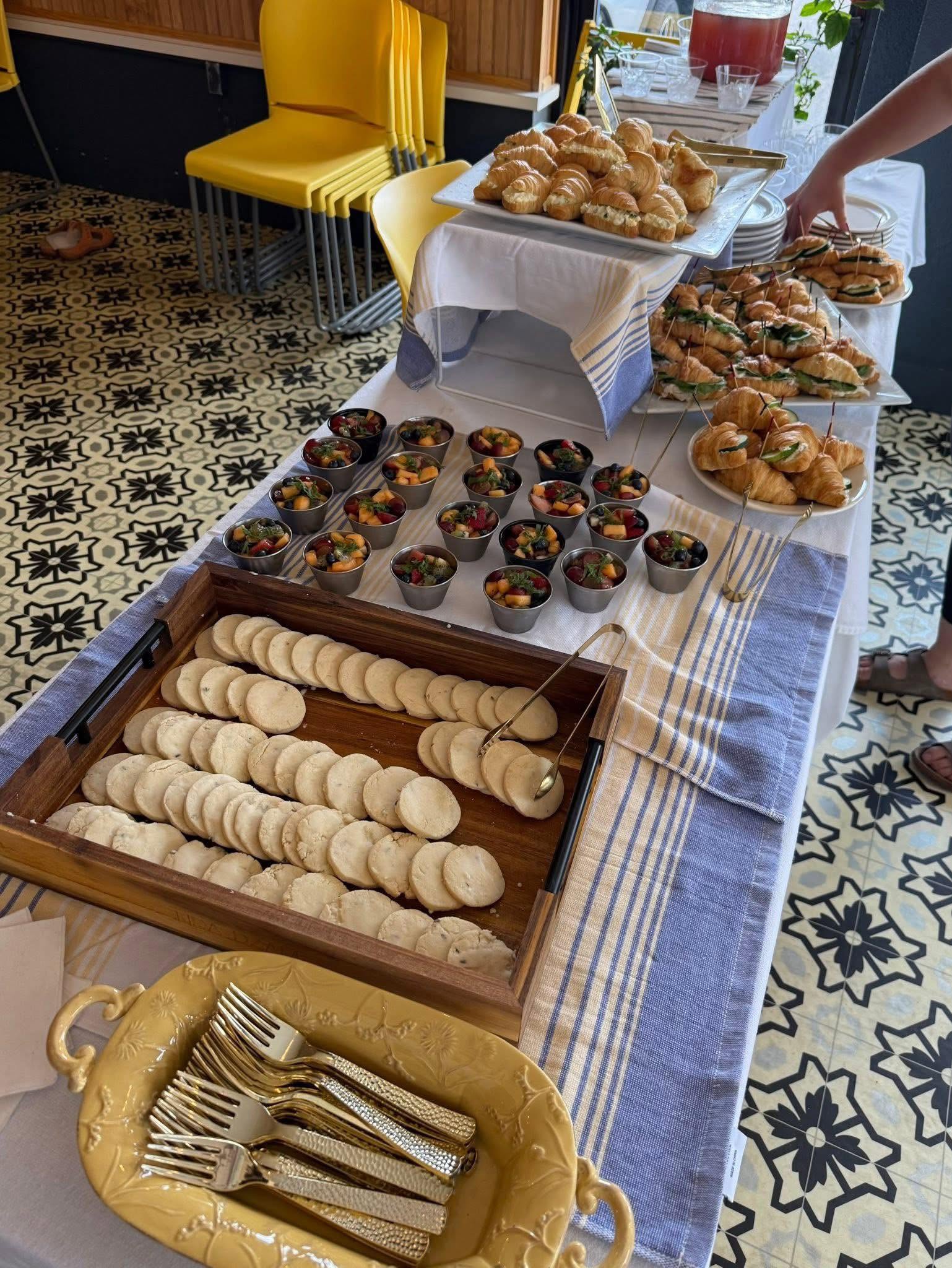 Catered table at Sunnyside Cafe with croissant sandwiches, fruit cups and cookies